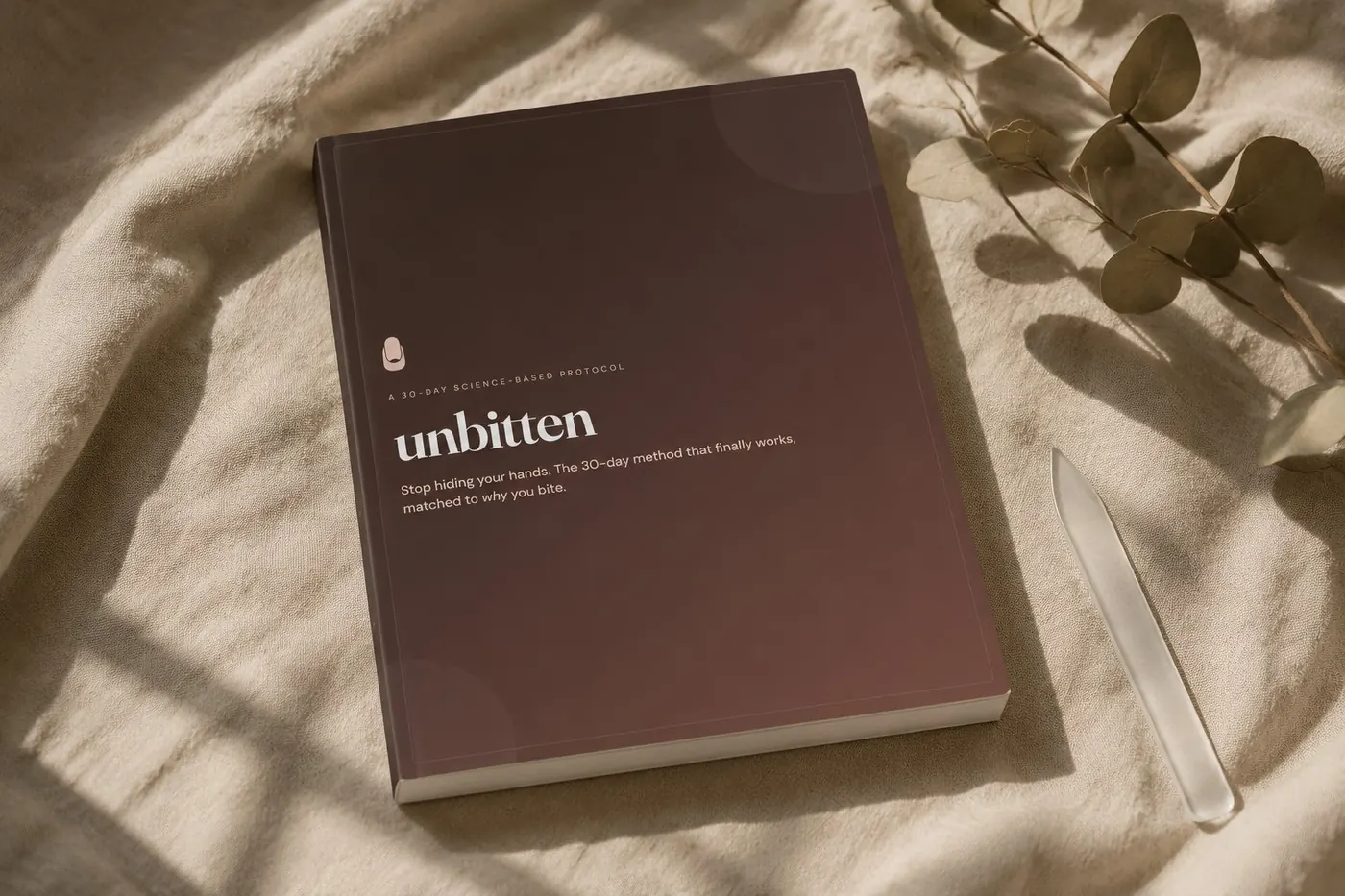 The Unbitten 30-day guide on warm linen, beside a glass nail file